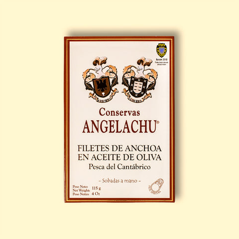 A tin of large Cantabrian anchovies in rectangular cream packaging with a brown border, against a pale yellow wood background.
