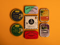Collection of premium tins on an orange table. There are sardines, octopus and mussels from Spain and France