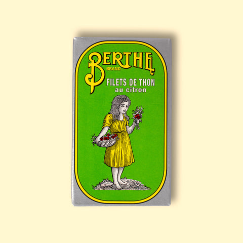 A rectangular box with a green background, silver border, and Berthe written in yellow above an image of a girl in a yellow dress
