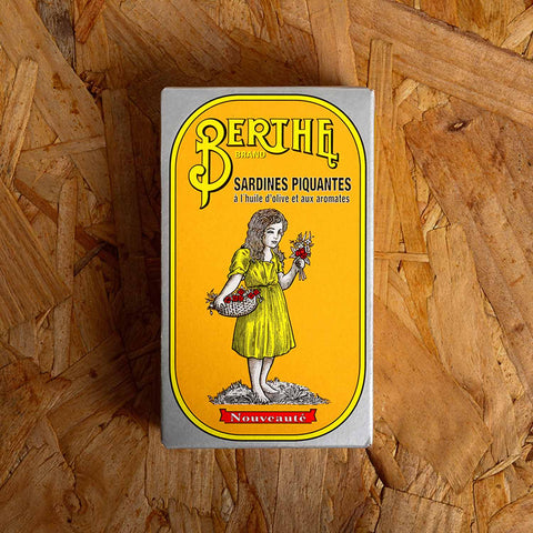 A tin of sardines in yellow card packaging with Berthe written in yellow above an image of a small girl in a yellow dress holding a bunch of flowers.