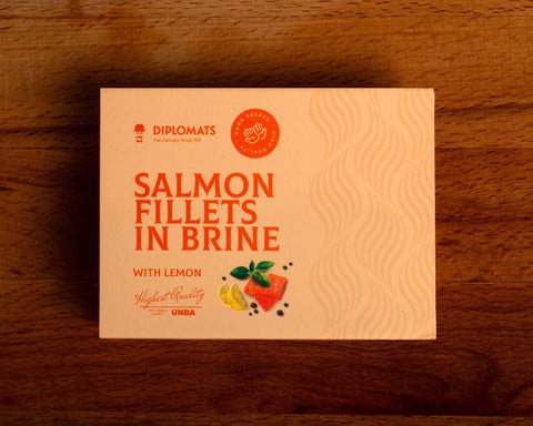 A tin of salmon fillets in pale orange packaging with orange lettering by a picture of two salmon fillets and two lemon wedges with a sprig of basil.