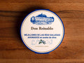 A round tin with a blue and white card wrap. There is an olive branch at the base, above it Don Reinaldo is written in gold lettering and there is a drawing of the cannery.