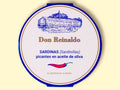A round tin with a white card wrap. The cover has a blue and gold border. Don Reinaldo is written in gold lettering below a drawing of the cannery. and above a red chilli pepper.
