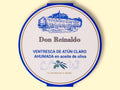 A round tin with a white card wrap. The cover has a blue and gold border. Don Reinaldo is written in gold lettering below a drawing of the cannery.