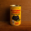 A yellow can of black olives, featuring an image of olives above a cartoon illustration of a fish skeleton, set against a wooden backdrop.