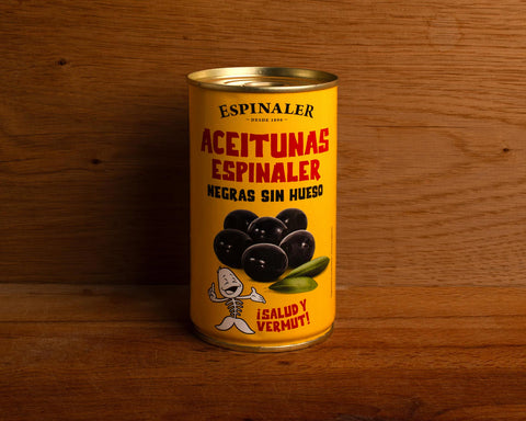 A yellow can of black olives, featuring an image of olives above a cartoon illustration of a fish skeleton, set against a wooden backdrop.