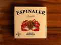 A tin of spider crab meat in square-shaped, cream-coloured card packaging with a picture of a 10-legged spider crab beneath the Espinaler logo in blue lettering. The can is against a wood background.