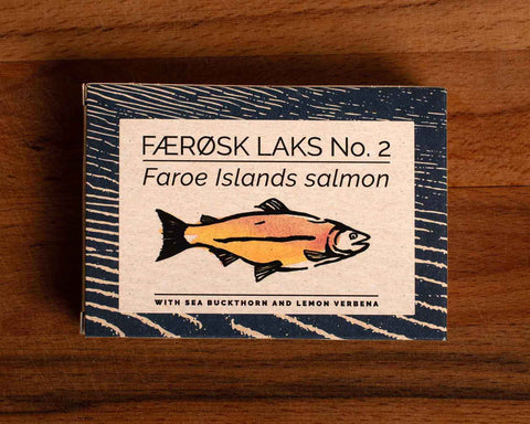 A tin of Faroe Islands salmon in white packaging with blue borders, featuring an illustration of a salmon with the description of sea buckthorn and lemon verbena below.
