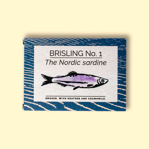 A tin of sprats in a rectangular box with a blue border and a painting of a purple sprat on the front, against a dark wood background.