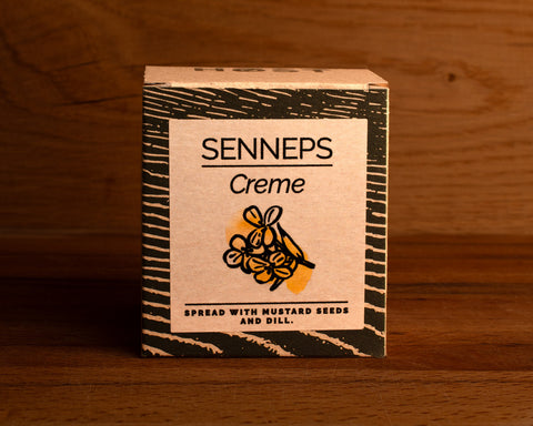A tin of mustard spread with dill in light grey square card packaging with blue borders, featuring an illustration of a dill flower.