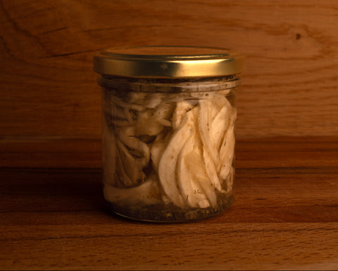 A transparent glass jar of pickled fennel with a golden cap, placed against a wooden background.