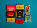 A selection of colourfully-packaged tinned mussels, sardines, tuna and mackerel against a blue background.