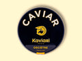A circular dark blue tin of caviar on a wood backdrop. Caviar is written in white lettering at the top of the tin, above the Kaviari logo: an illustration in gold of a sturgeon fish above Kaviari Paris also in gold lettering. The tin is sealed with a yellow and blue label reading Osciètre prestige.