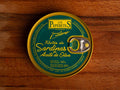 A tin of boneless sardines in green packaging with golden borders, featuring the Los Peperetes label at the top, set against a wooden backdrop.