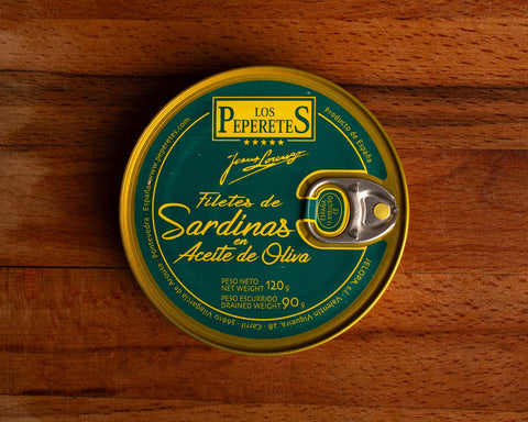 A tin of boneless sardines in green packaging with golden borders, featuring the Los Peperetes label at the top, set against a wooden backdrop.