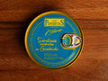 A tin of sardines in escabeche, featuring light blue packaging with golden corners and the Los Peperetes label at the top, set against a wooden backdrop
