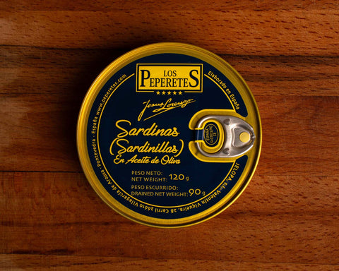 A dark blue tin with golden borders containing small sardines, featuring the Los Peperetes label at the top, set against a wooden backdrop.