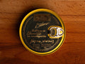 Ventresca in jersey butter, packaged in a circular chocolate-brown tin with a golden border and golden lettering, against a wooden backdrop.