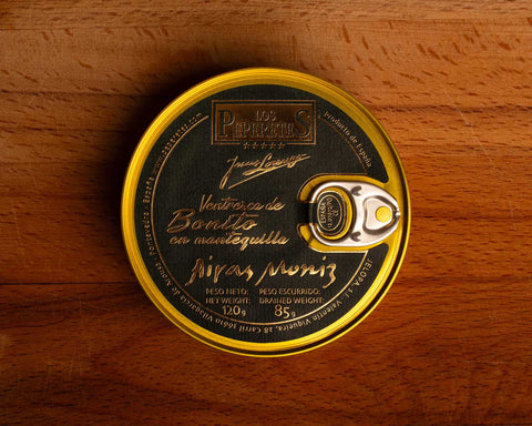 Ventresca in jersey butter, packaged in a circular chocolate-brown tin with a golden border and golden lettering, against a wooden backdrop.