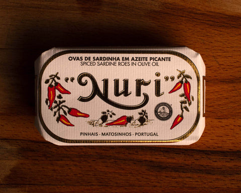 A tin of spicy sardine roe in white and gold paper packaging with illustrations of red chillies beneath the Nuri logo.