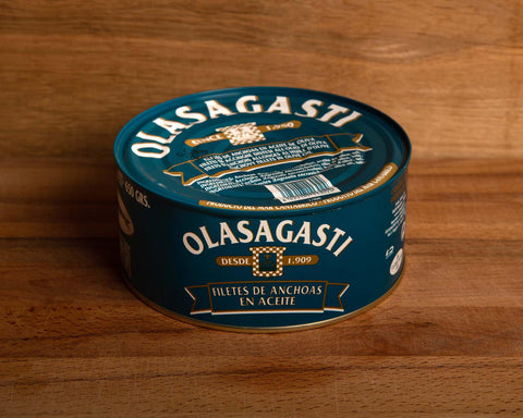 A tin of anchovy fillets in a large round dark blue can, set against a wooden backdrop.