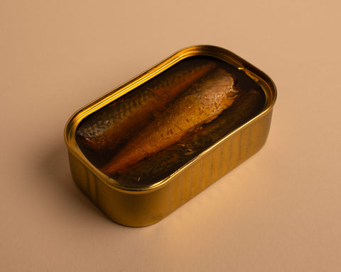 A golden tin with three mackerel pieces in olive oil, against a pale background.