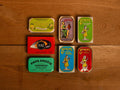 A selection of colourfully-packaged tinned sardines, tuna, squid and mussels against a wood background.