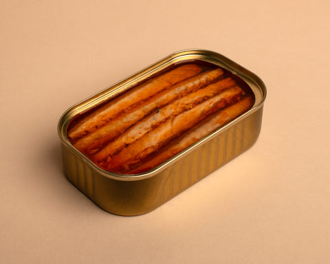 A golden tin with five mackerel fillet pieces in spicy tomato olive oil, against a pale background.