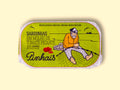 A tin of sardines in a green paper wrap with an image of a fisherman mending a net by some tomatoes and a red chilli pepper. The tin is on a yellow wood backdrop.