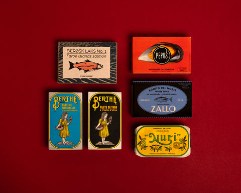 A selection of colourfully-packaged tinned
sardines, tuna, mackerel, salmon and mussels against a red background.