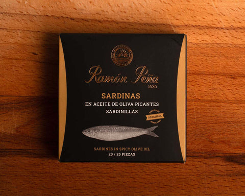 Spicy sardines in black and gold card packaging. Ramón Peña is written in gold lettering above a silver-grey image of a sardine.