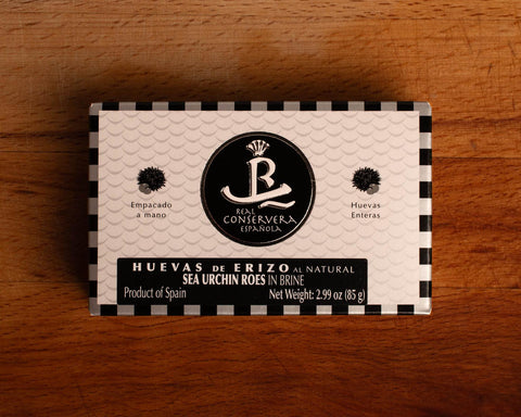 A rectangular tin of sea urchin roe in brine, with white and black packaging, displaying sea urchin illustrations next alongside the Real Conservera logo.