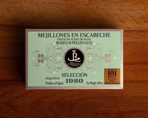 A rectangular tin of mussels in pickled sauce in mint green packaging with grey borders, set against a wooden backdrop.