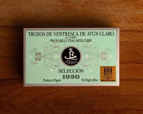 A rectangular tin of tuna belly with curry in mint green packaging with grey borders, set against a wooden backdrop.