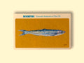 A can of anchovies in off-white card packaging with a painting of a long blue, green and silver fish against a yellow background below Rockfish Plymouth anchovies in olive oil written in blue lettering.