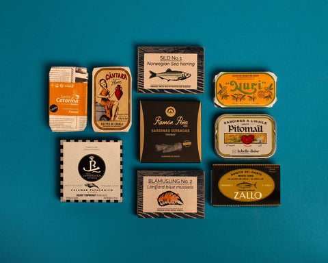 A selection of colourfully-packaged tinned mussels, squid, sardines, herring, tuna and mackerel against a blue background.