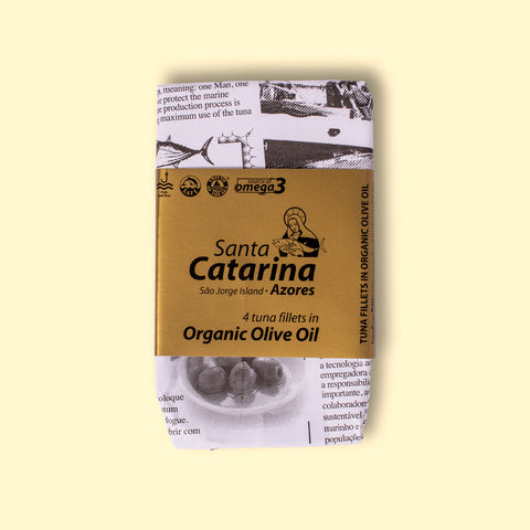 A tin of Santa Catarina tuna in black and white packaging with a gold label against a yellow wood background