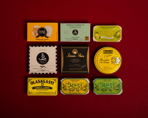 A selection of colourful tinned fish displayed against a dark red background, featuring sardines, cockles and squid varieties.