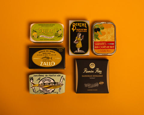A selection of colourfully packaged tins of sardines and tuna against a yellow background.