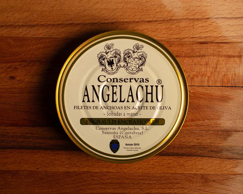 A tin of 32 cantabrian anchovy fillets in a circular white container with golden borders, set against a wooden backdrop.