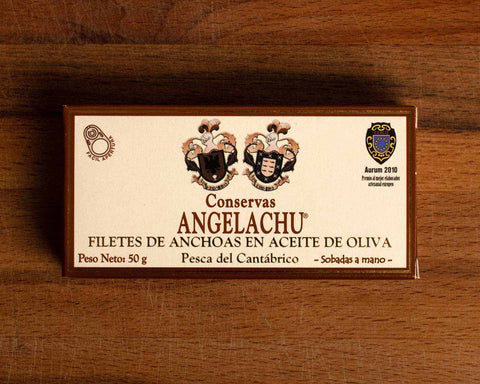 A tin of anchovies in a rectangular brown and cream box against a wood background