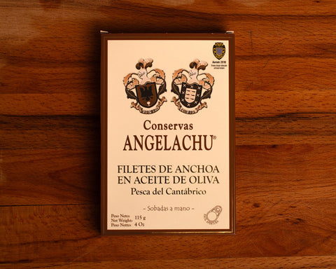 A tin of large Cantabrian anchovies in rectangular cream packaging with a brown border, against a wood backdrop.