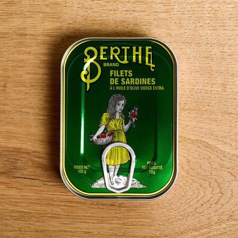 A bottle-green tin with an image of a girl in a yellow dress laminated onto the front of the tin 