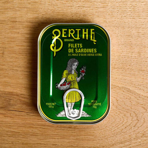 A bottle-green tin with an image of a girl in a yellow dress laminated onto the front of the tin