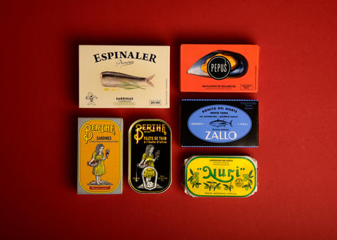 Six brightly packaged tins of fish against a red background