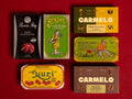 Six vintage Spanish tinned fish boxes arranged on a solid red background. The boxes feature retro designs with illustrations .