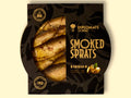 Smoked sprats in pistachio oil, shown in partially open black packaging, with the golden-brown fish visible inside.