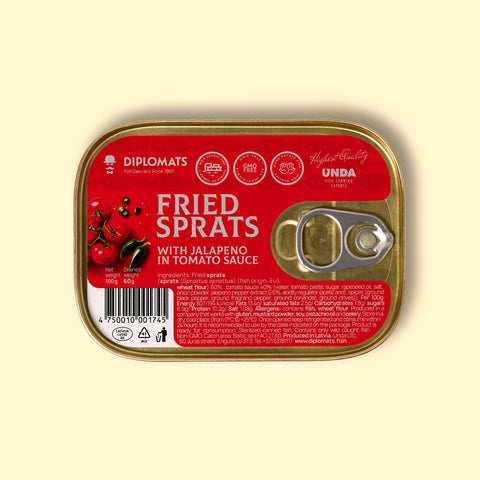 A golden-coloured rectangular tin with a silver ring-pull on the right. The tin is on a pale yellow background. The tin has a red sticker covering its surface with "Fried sprats with jalapeño in tomato sauce" written in white lettering by an image of some tomatoes on the vine and two jalapeño peppers. The ingredients and nutrients are written at the bottom of the label in small white type.