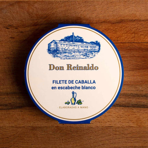 A round tin with white card packaging. The card has a blue and gold border. Don Reinaldo is written in gold lettering with an image of the cannery above.