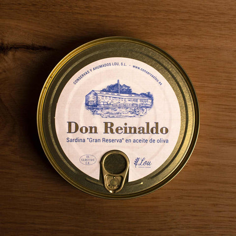 A round gold-coloured tin with a round white sticker on the front. Don Reinaldo is written in gold lettering on the sticker beneath a drawing of the cannery on the banks of the Galician Rías  